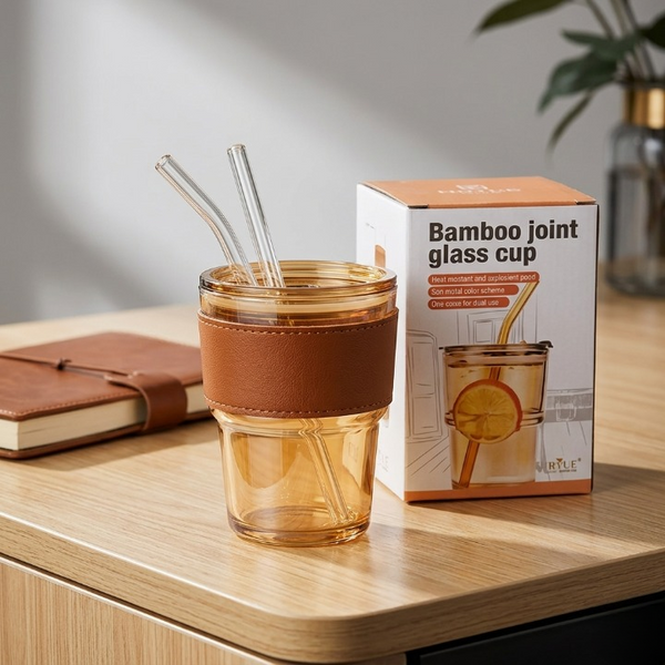 The Range Studio signature amber glass cup and product box arranged elegantly next to a leather journal notebook on a wooden desk.