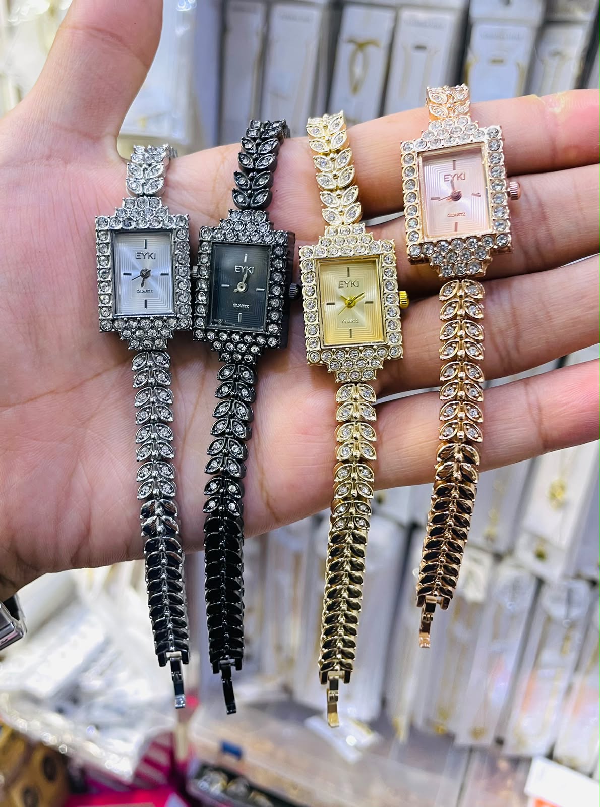 A hand displaying the four colorways of the Range Studio Leaf-Link Rhinestone Watch in Silver, Onyx Black, Imperial Gold, and Blush Rose Gold.