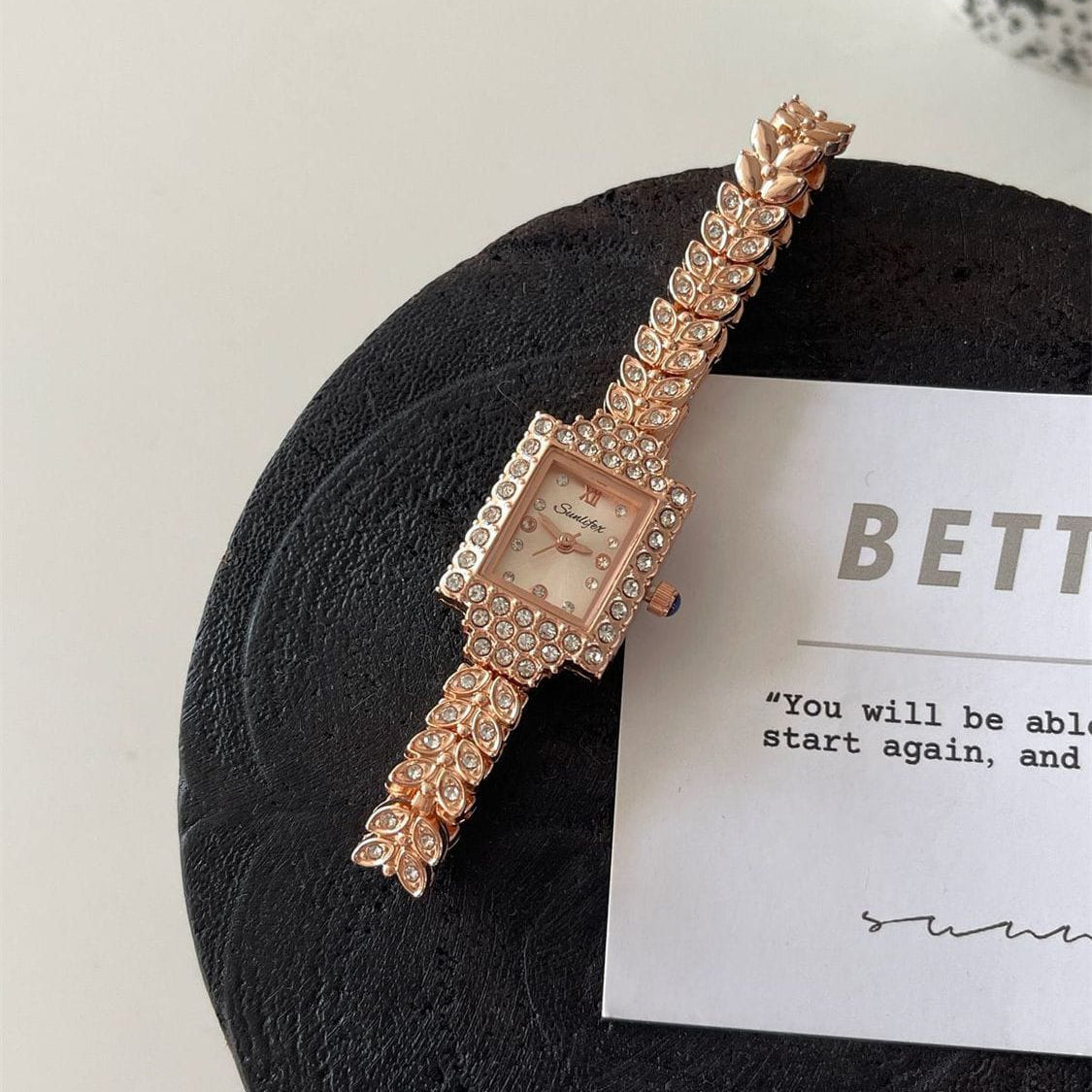 Minimalist presentation of the Blush Rose Gold Range Studio leaf-link bracelet watch styled on a matte black stone plaque pedestal.
